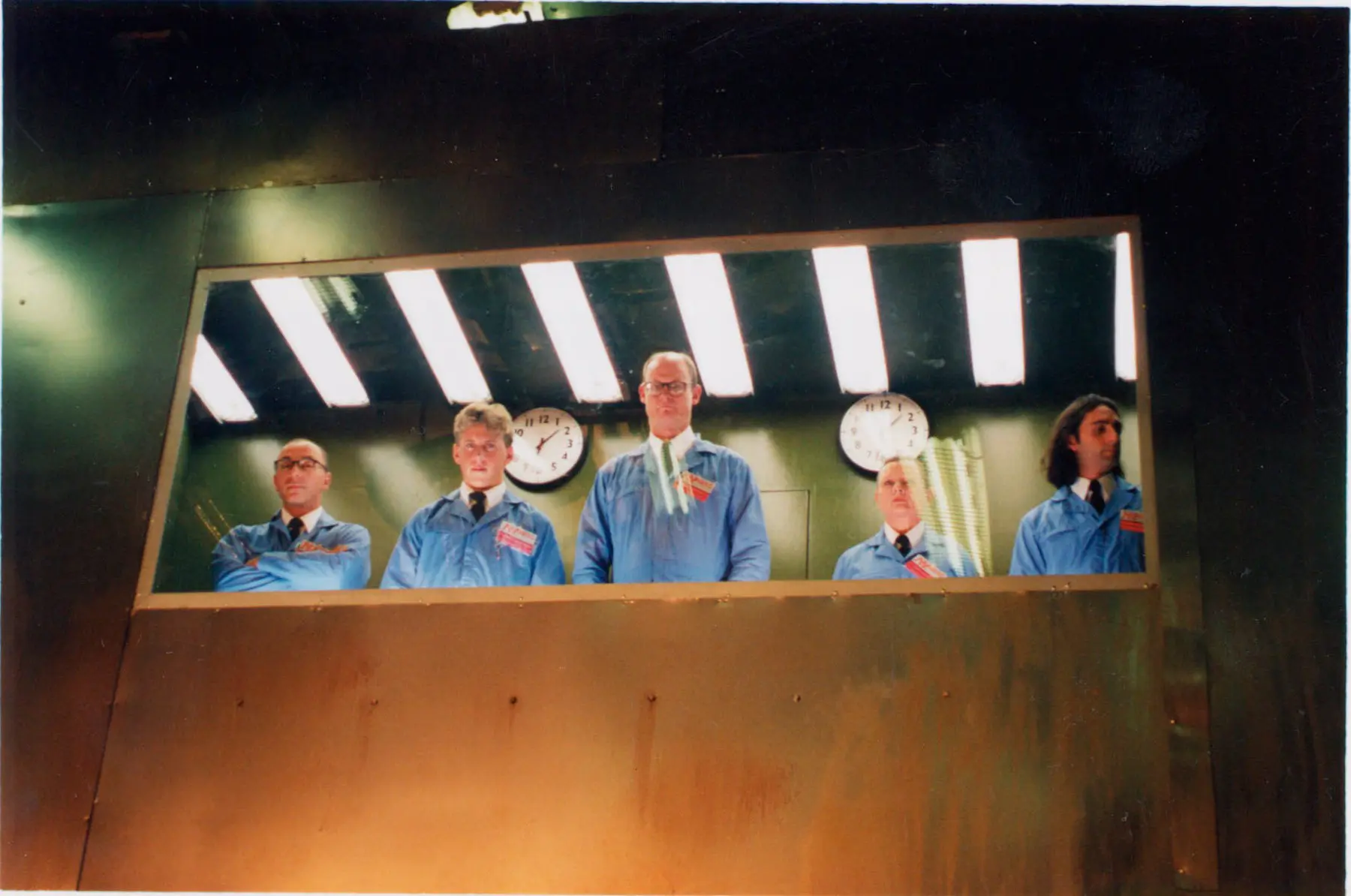 Five people in blue uniforms behind glass.
